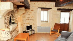 A cozy living room with a stone wall, a fireplace, a sofa, a chair, and a small table. - Charming 18th Century Gîte with Garden, Near Castles & Vineyards, Pet Friendly (Betz-le-Château)