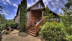 A log cabin with a porch, wooden steps, and a wheel chair.