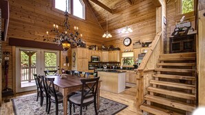 A spacious wooden cabin with a dining area, kitchen, and a staircase.