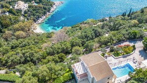 Vista aérea de uma propriedade costeira com piscina, rodeada por vegetação exuberante e um mar azul cristalino.