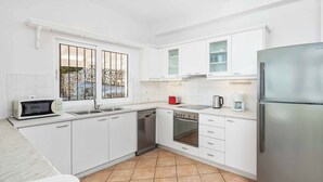 Uma cozinha moderna com armários brancos, uma geladeira de aço inoxidável, micro-ondas, lava-louças e forno.