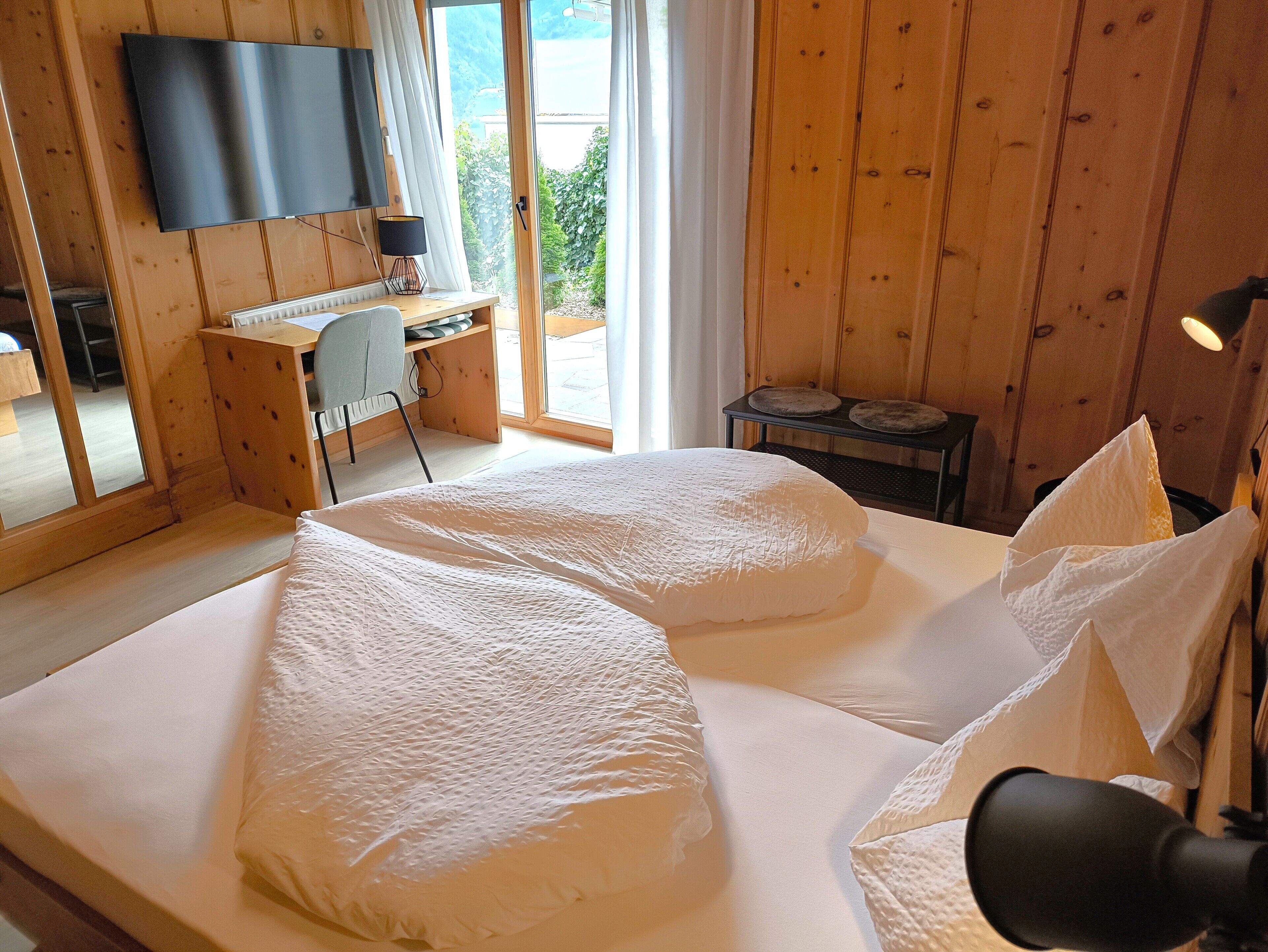 Un dormitorio con cama, escritorio, silla, televisor y vistas al exterior.