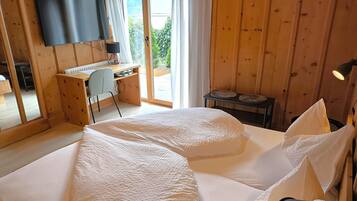 Un dormitorio con cama, escritorio, silla, televisor y vistas al exterior.