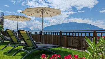 Una terrazza con due poltrone e due ombrelloni, vista su un corpo d'acqua e montagne.