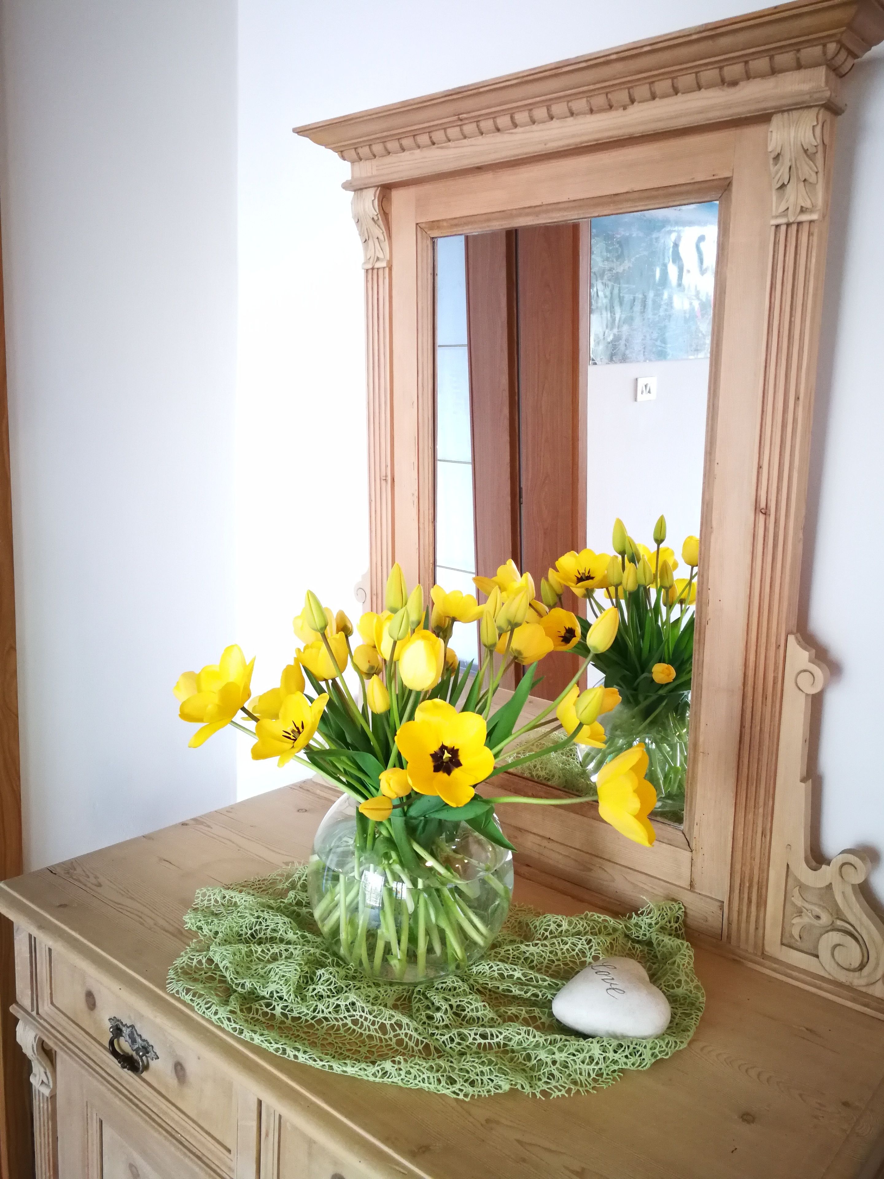Ein hölzerner Nachttisch mit einer Vase voller gelber Blumen und einem herzförmigen Stein.