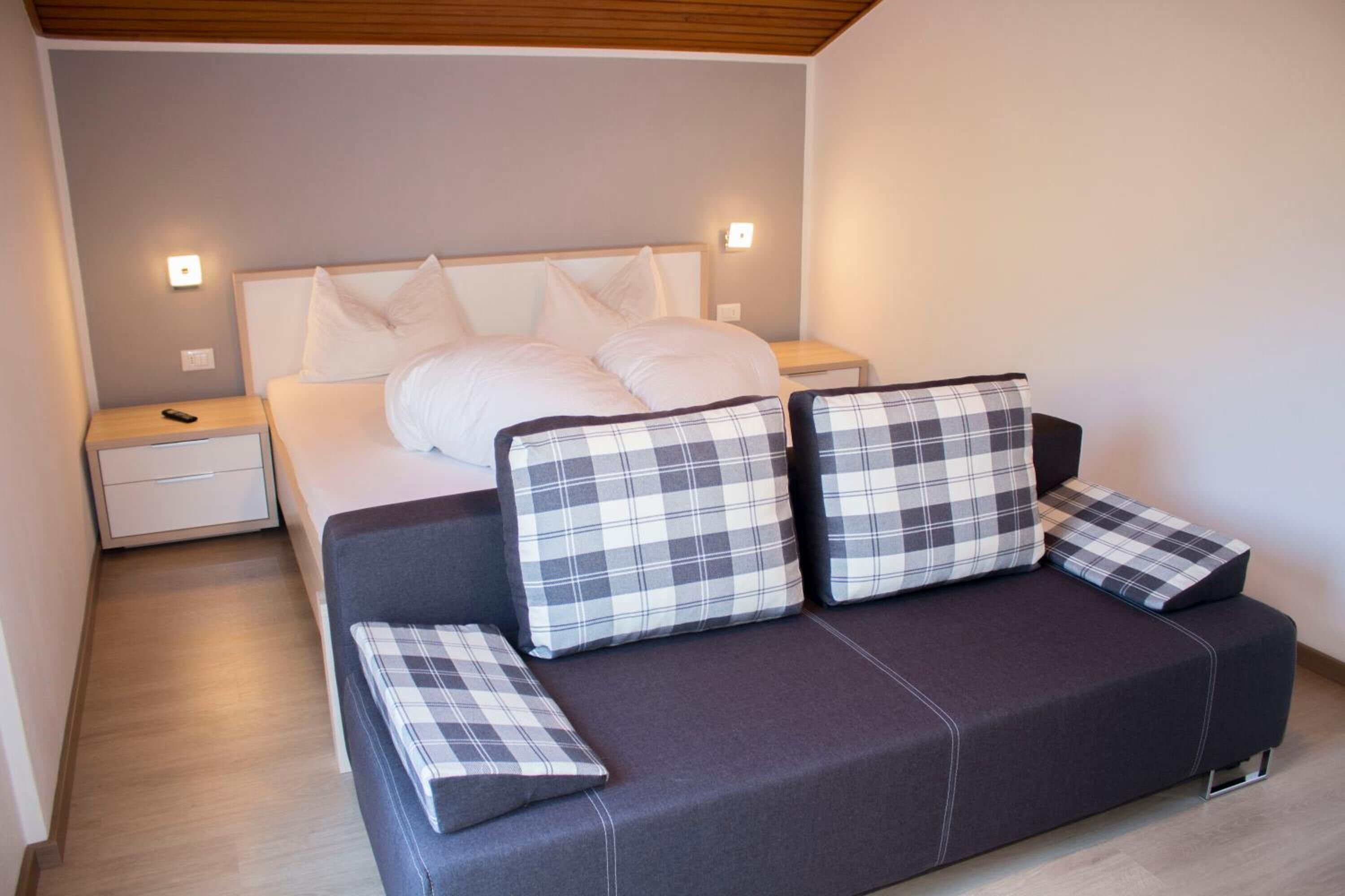 A modern bedroom with a bed, a dark sofa, and two bedside tables.