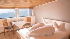 A bedroom with a bed, a desk, two chairs, a radiator, and a window with a view. - Schenna Garni Eden Bed & Breakfast (Schenna)