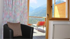 A room with a view of mountains, a black chair with a cushion, and a wooden deck with a red chair. - Schenna Garni Eden Bed & Breakfast (Schenna)