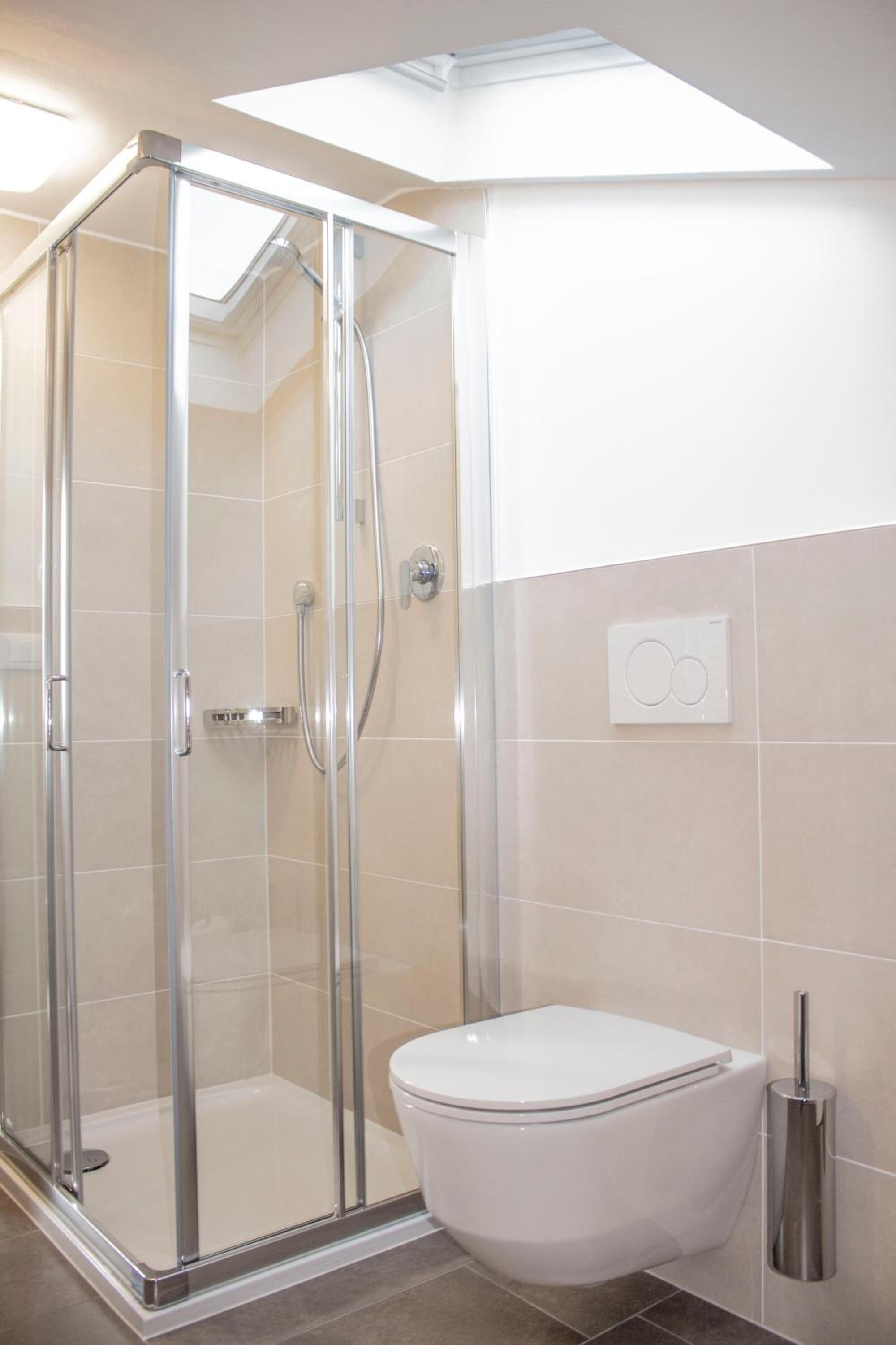 Een moderne badkamer met een douche met glazen wand, een wit toilet en een zichtbare lichtschakelaar aan de muur.
