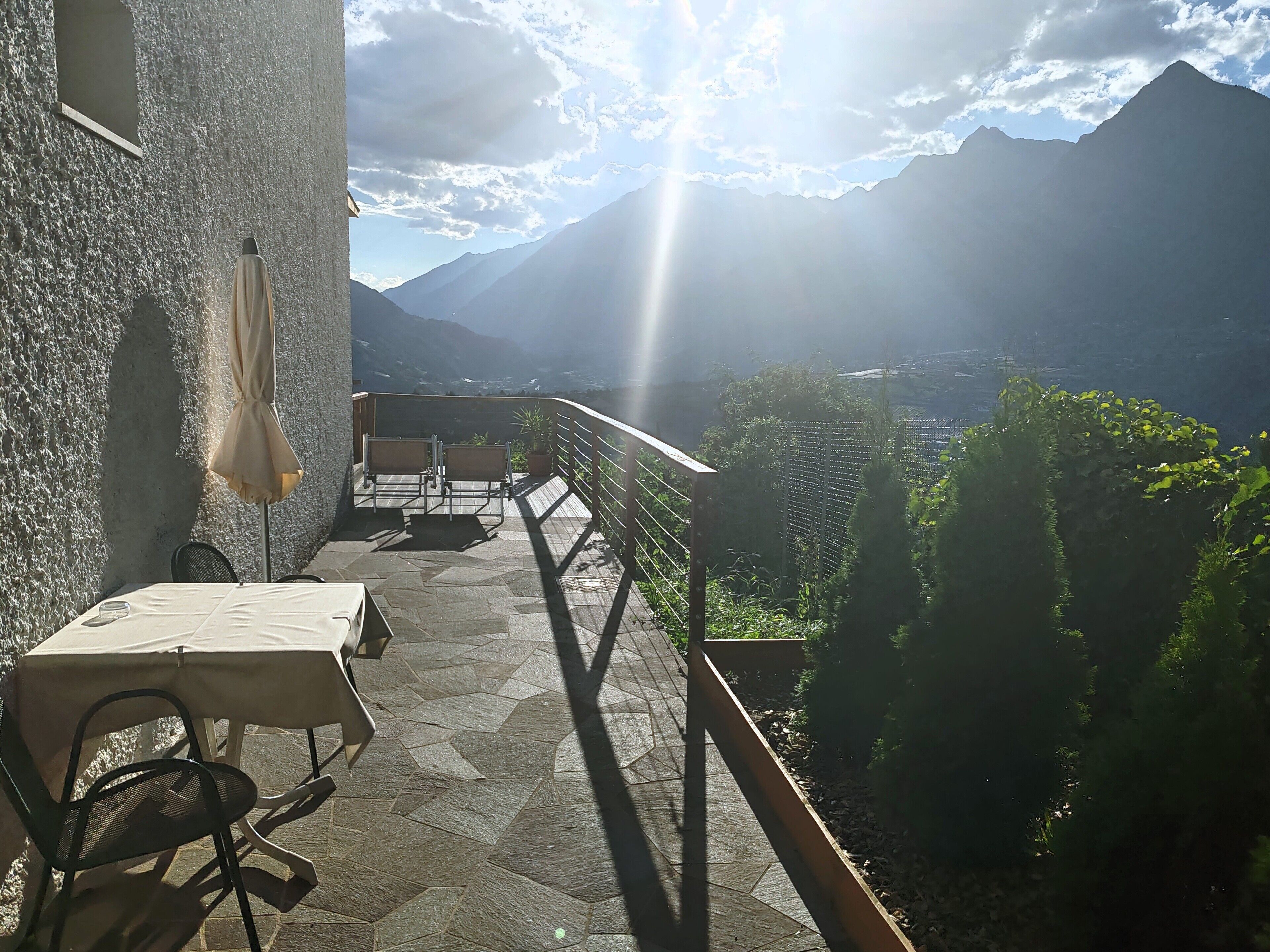 A terrace with a table and chairs, overlooking a mountainous landscape.