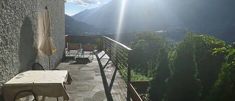 A terrace with a table and chairs, overlooking a mountainous landscape.