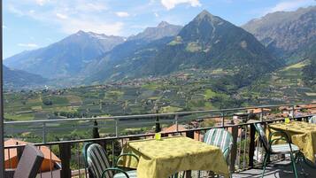 Una terrazza con posti a sedere all'aperto, affacciata su un paesaggio montuoso con un villaggio in basso.