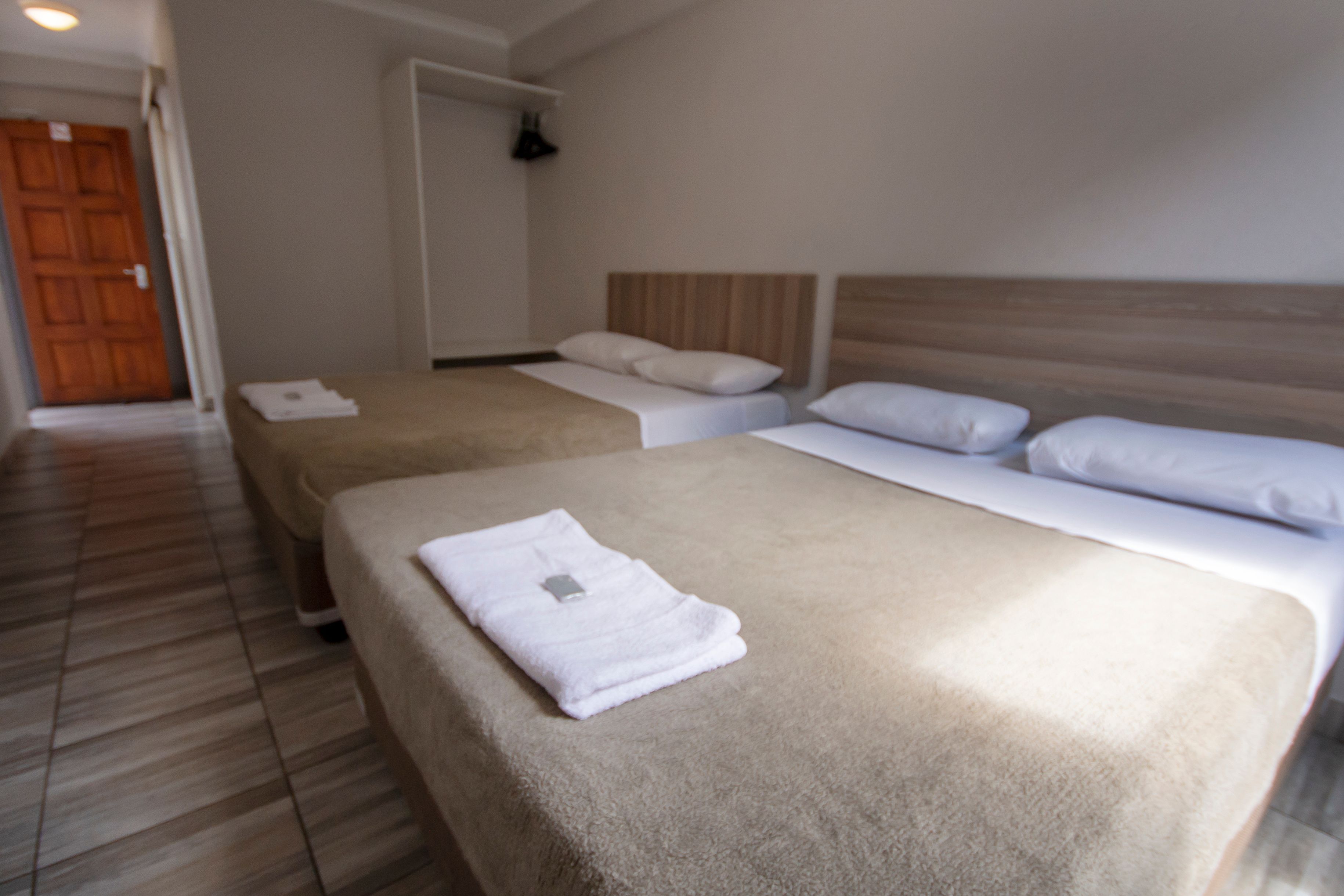 A hotel room with two beds, a wooden headboard, and a door in the background.