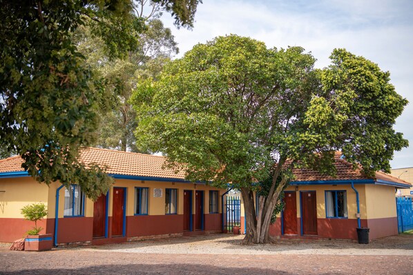 Um edifício de dois andares com telhado de azulejos, uma árvore central e um portão azul.