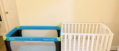 Un parc pour bébé et un berceau dans une pièce dont le sol est recouvert de parquet et qui possède une porte blanche.
