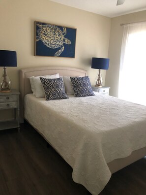 Un dormitorio con una cama grande, dos mesitas de noche, un cuadro de una tortuga colgado en la pared y una ventana con cortinas.