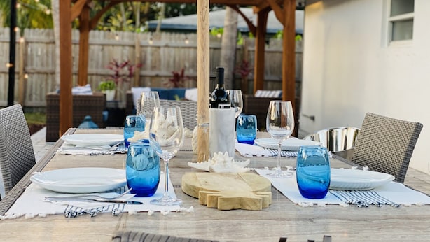 An outdoor dining area with a wooden pergola, string lights, and a table set for four with blue glassware and a bottle of wine. - Family/ Kid Friendly Retreat Near the Beach, Atlantic Ave, Downtown Delray & FAU (Delray Beach)