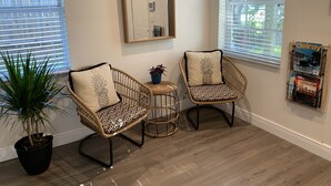 A room with two wicker chairs, one with a pineapple pillow and the other with a leopard print pillow, a small table with a plant, and a magazine rack on the wall. - Family/ Kid Friendly Retreat Near the Beach, Atlantic Ave, Downtown Delray & FAU (Delray Beach)