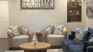 A living room with two armchairs, a sofa, a coffee table, and a ceiling fan. A sign on the wall reads "BEACHHOUSE". - Family/ Kid Friendly Retreat Near the Beach, Atlantic Ave, Downtown Delray & FAU (Delray Beach)