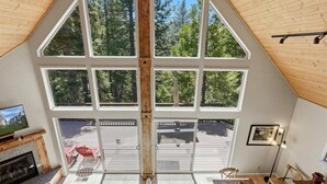 Ein Zimmer mit hohen Decken, großen Fenstern, einem Kamin und Blick auf eine Terrasse und Bäume.