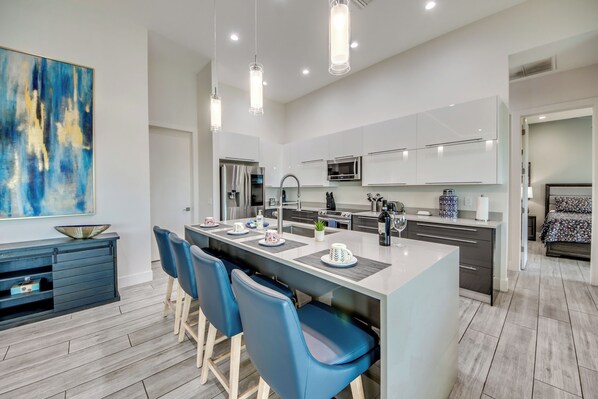 A modern kitchen with a central island, bar stools, and a large abstract painting on the wall.
