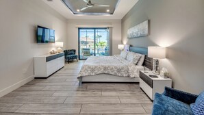 A modern bedroom with a bed, bedside tables, a TV, and a ceiling fan.