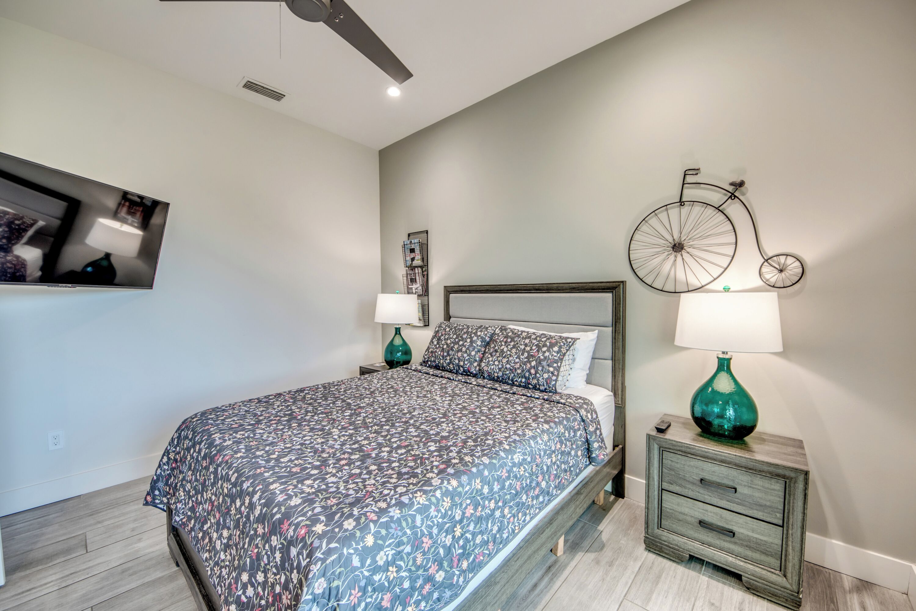 A bedroom with a bed, nightstands, a bicycle wall art, and a ceiling fan.