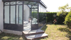 Uma estufa com paredes de vidro, degraus que levam a um espaço de estar com cadeiras brancas e vista para o jardim.