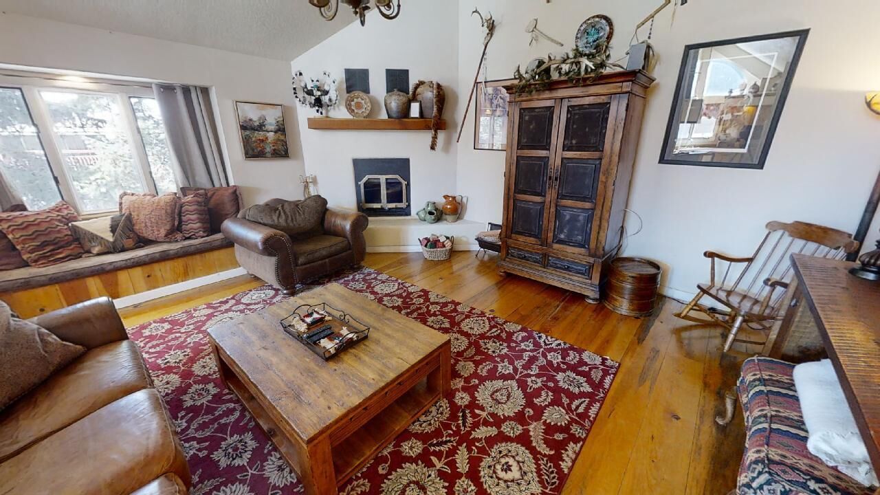 Un salon chaleureux avec un canapé en cuir, une table basse en bois et un tapis à motifs. On y trouve une cheminée, un meuble décoratif et une fenêtre donnant sur les arbres.