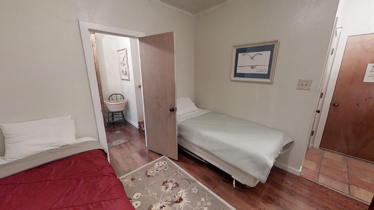 A room with a bed, a small table, and a chair. There is a door leading to another room.
