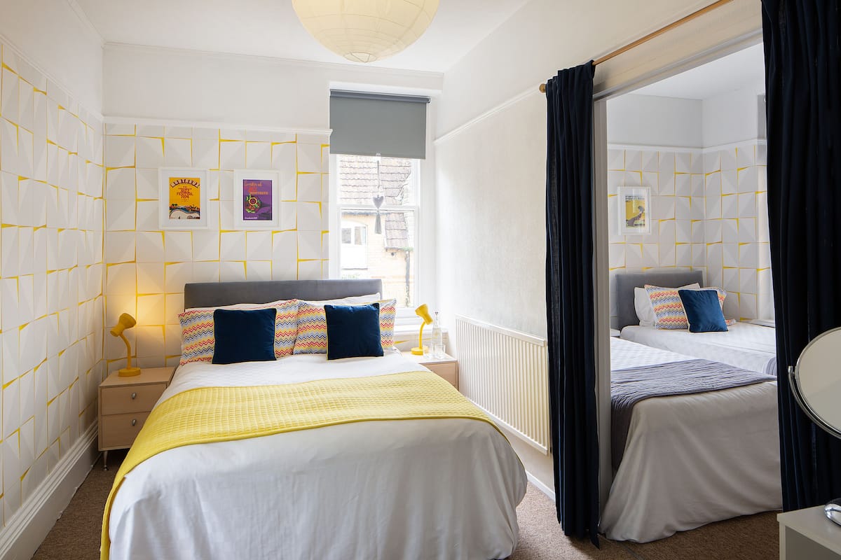 Hotellihuone, jossa on suuri sänky, pienempi sänky, yöpöytä lampun kanssa, peili ja ikkuna, josta on näkymä rakennuksiin.