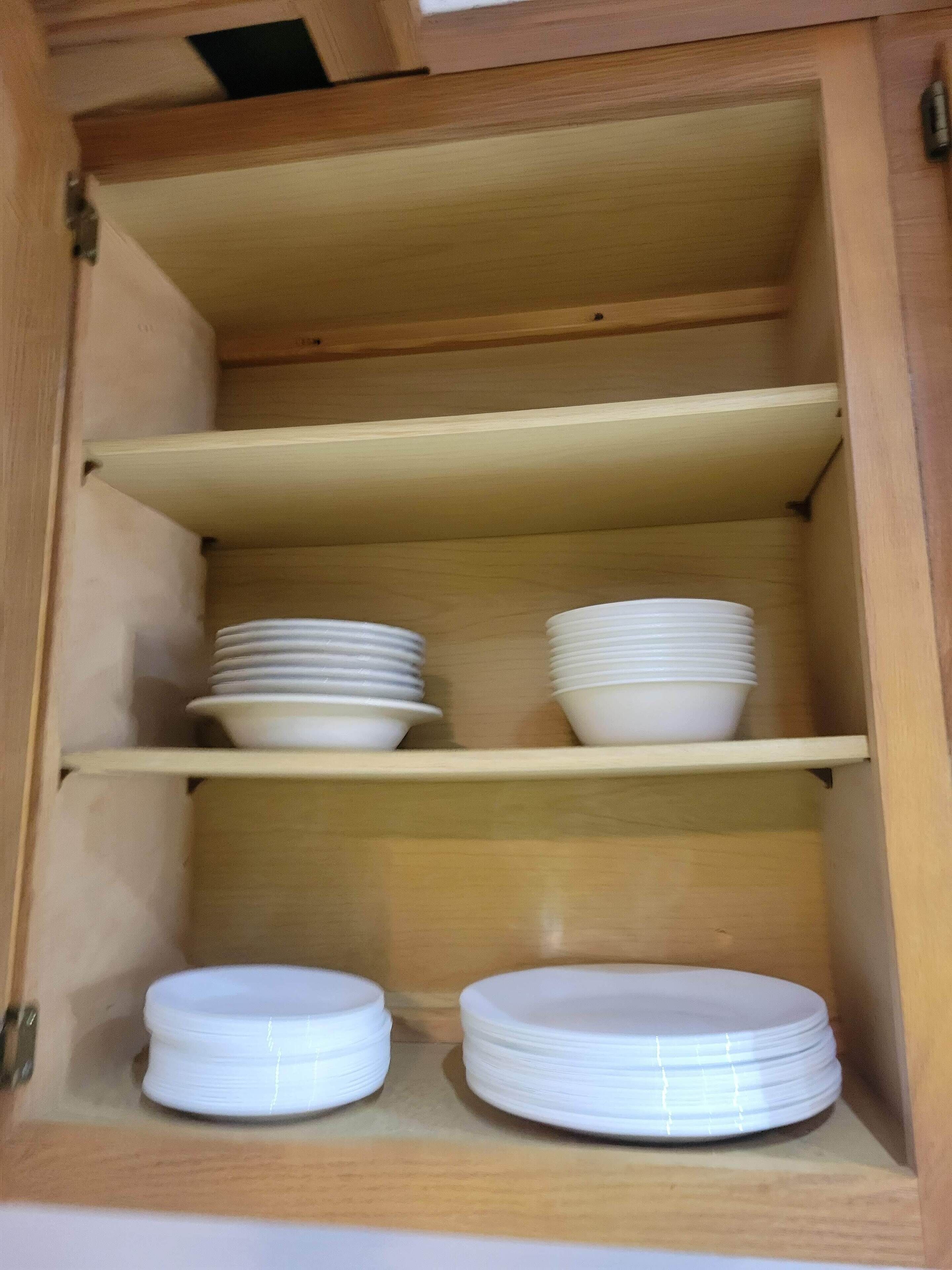 Een houten kast met drie planken, elk gevuld met stapels witte borden.