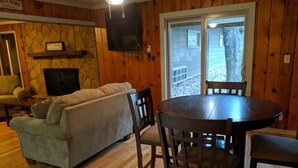 A cozy living room with a stone fireplace, wooden walls, a sofa, and a dining table with chairs.