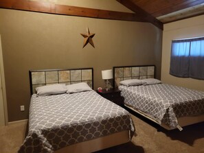 A room with two beds, each with a patterned bedspread and pillows, a wooden star decoration on the wall, and a nightstand with a lamp.