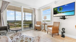 Una habitación con balcón, mobiliario de mimbre, televisor y un sofá estampado con conchas marinas.