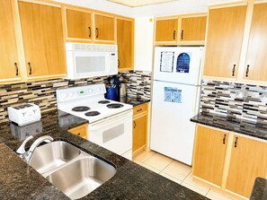 A kitchen with wooden cabinets, a white stove, a microwave, and a refrigerator. - Baywatch 322 (North Myrtle Beach)