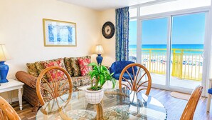 Un salon avec une table en verre, des chaises en bois, un canapé et une vue sur la plage.