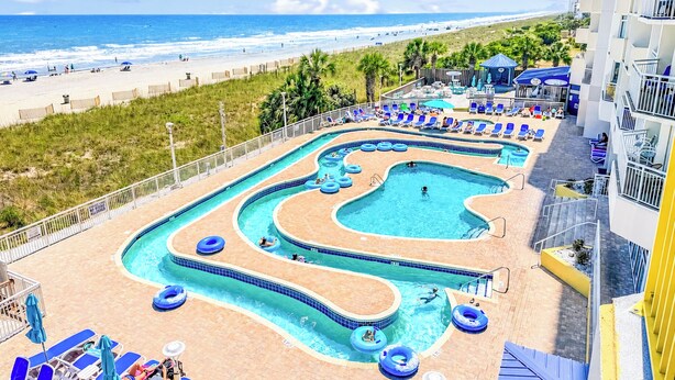 Un espace piscine comprenant plusieurs piscines, des chaises longues et une vue sur la plage.