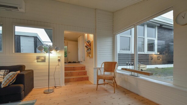 A cozy room with a wooden floor, a black sofa, a floor lamp, and a chair by a large window. - Cozy home in Knebel with house sea view (Knebel)
