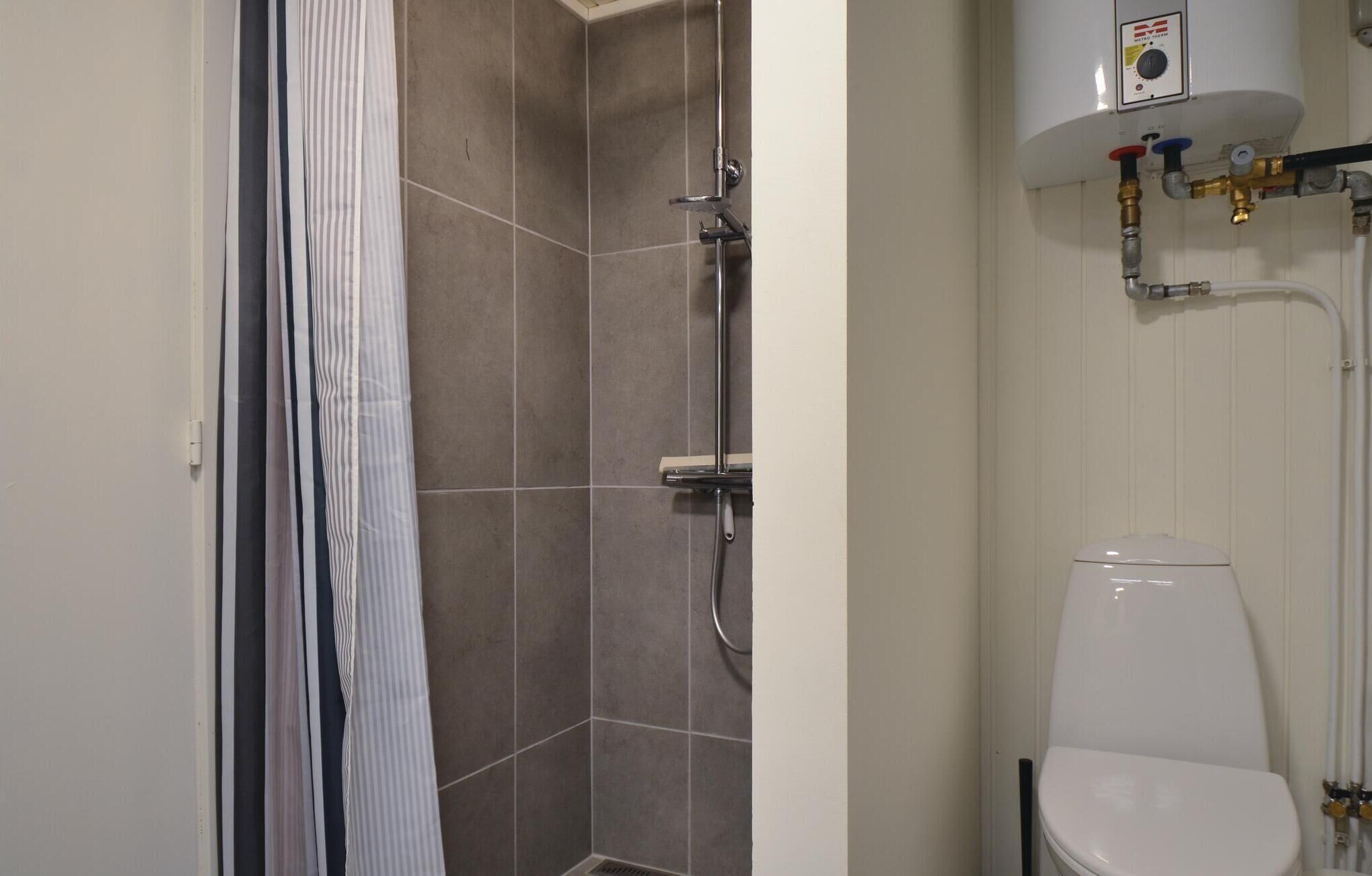 Een badkamer met douche, toilet en een boiler.