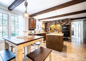 Une cuisine dotée d’un grand îlot central, de poutres en bois, d’un mur en briques et d’appareils électroménagers modernes.