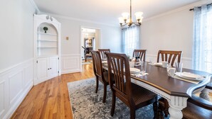 A dining room with a wooden table, chairs, and a chandelier. There is a white shelving unit and a rug on the floor. - The Evergreen Home In Lancaster County PA. (Bird in Hand)