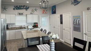 Una cocina moderna con armarios blancos, encimera de granito y comedor con mesa y sillas oscuras.