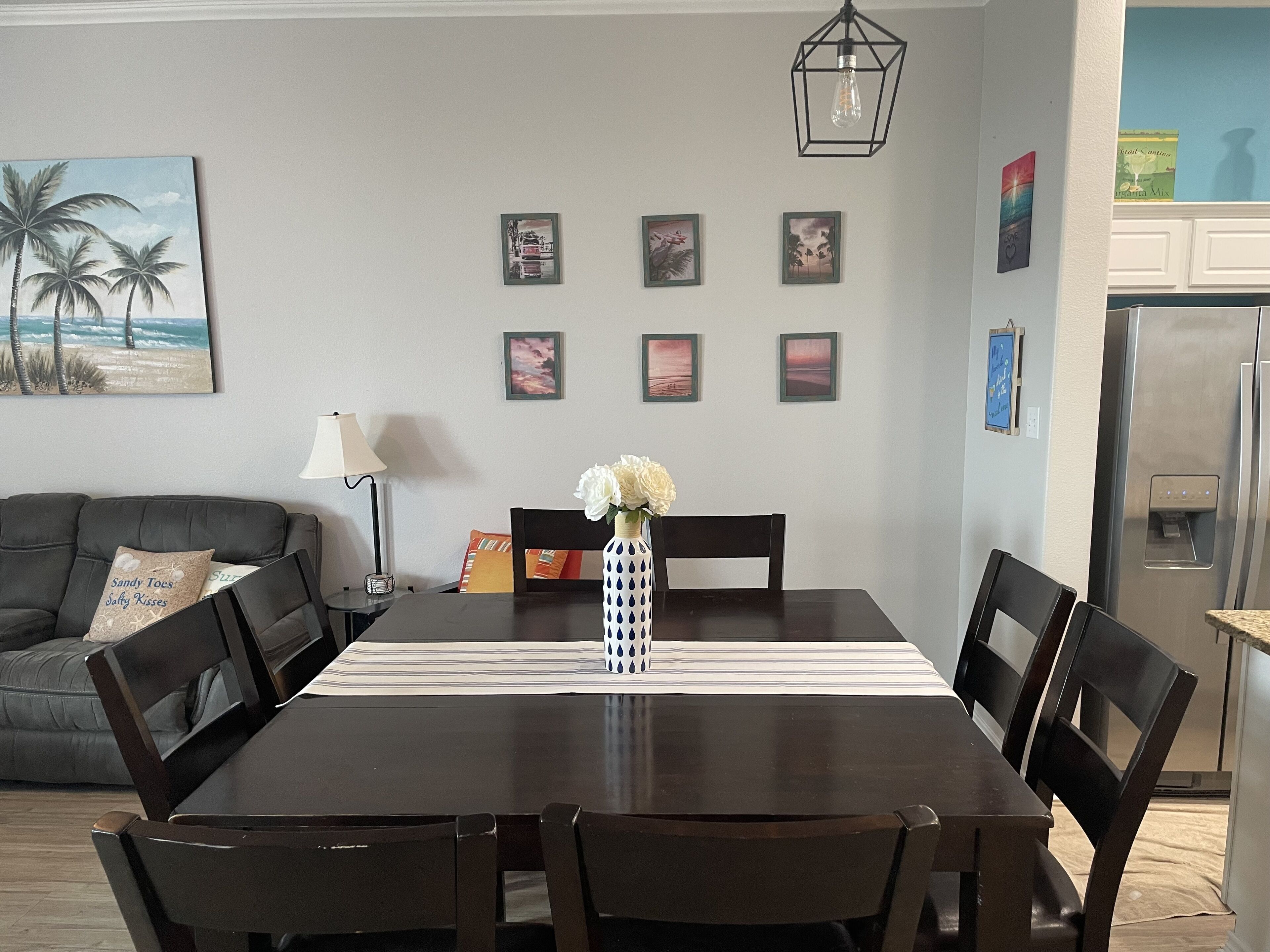 A dining area with a dark wooden table, six chairs, a vase with white flowers, and a lamp.