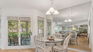 A spacious dining area with a glass table surrounded by wicker chairs, large windows, and a view of the outdoors. - Hidden Dunes First Floor Cottage Steps from the Pool, Rare 1 Bedroom, 2 Bathroom (Miramar Beach)