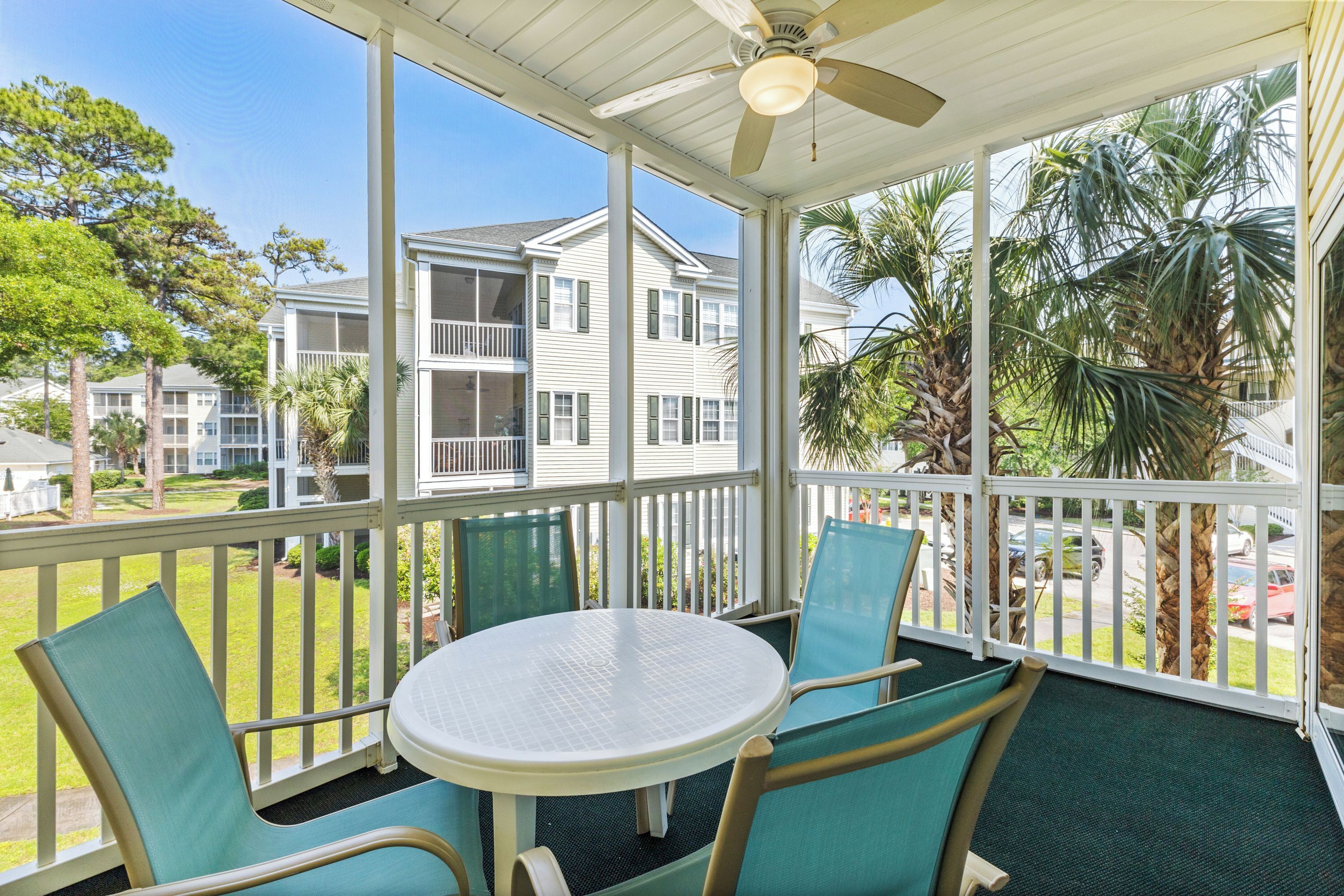 A covered outdoor area with a table and chairs, a ceiling fan, and a view of neighboring buildings and palm trees.