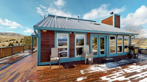 Une cabane dotée d’une terrasse, de grandes fenêtres et d’une cheminée.