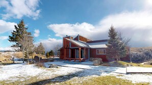 Une maison moderne en bois dotée d’une grande terrasse, entourée d’un paysage enneigé et d’arbres.