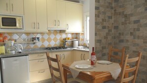 Een kleine keuken met een magnetron, fornuis en spoelbak. Er staat een eettafel met stoelen en een fles wijn.