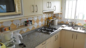 Een keuken met een magnetron, fornuis, spoelbak en diverse keukenbenodigdheden op het aanrecht.